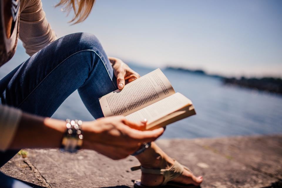 Woman reading a book outdoors by the water