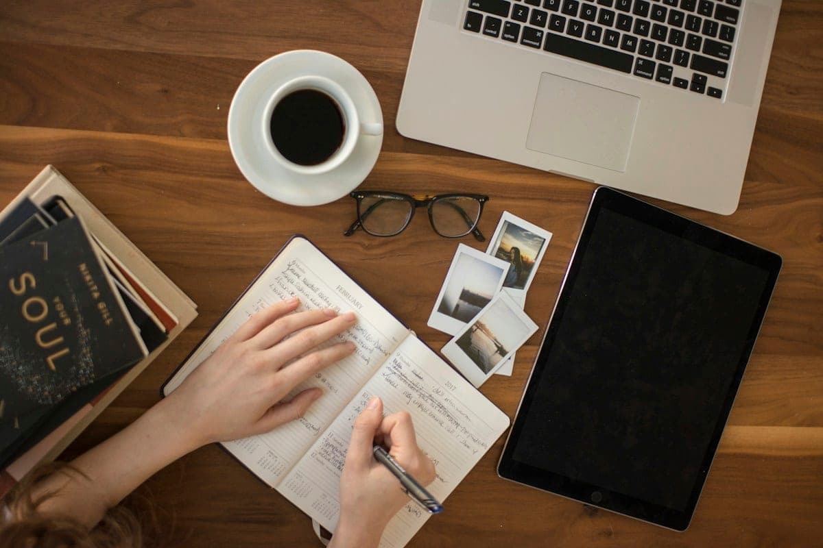 Hands writing notes in a notebook next to a laptop