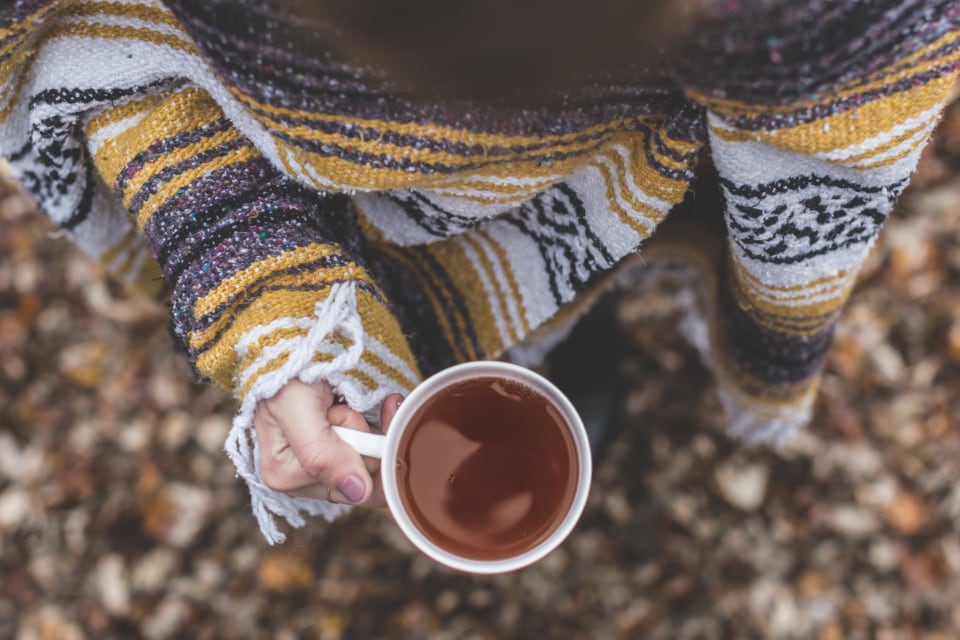 Hands holding a warm cup of tea over a knitted blanket