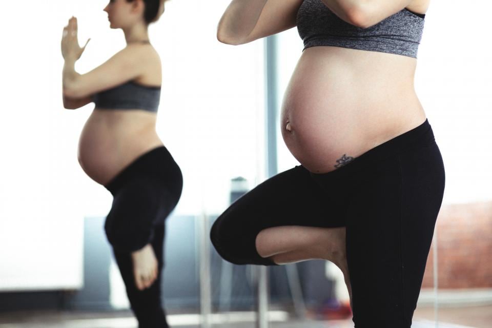 Two pregnant women balancing in a yoga pose